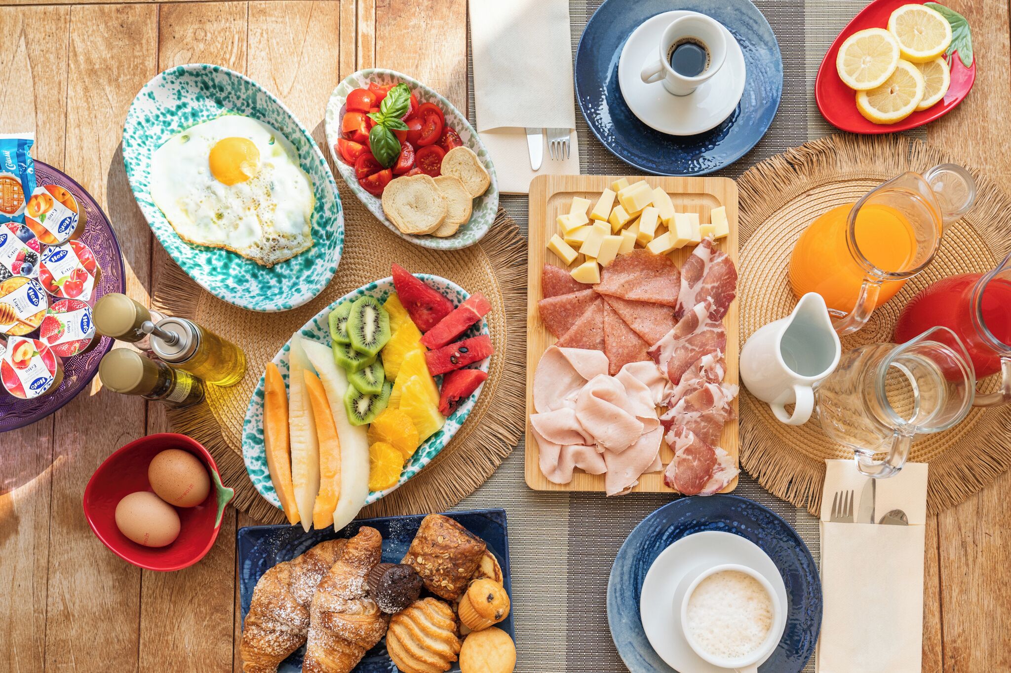 Una mesa de madera con una variedad de alimentos para el desayuno: huevos, frutas, carnes y bebidas.