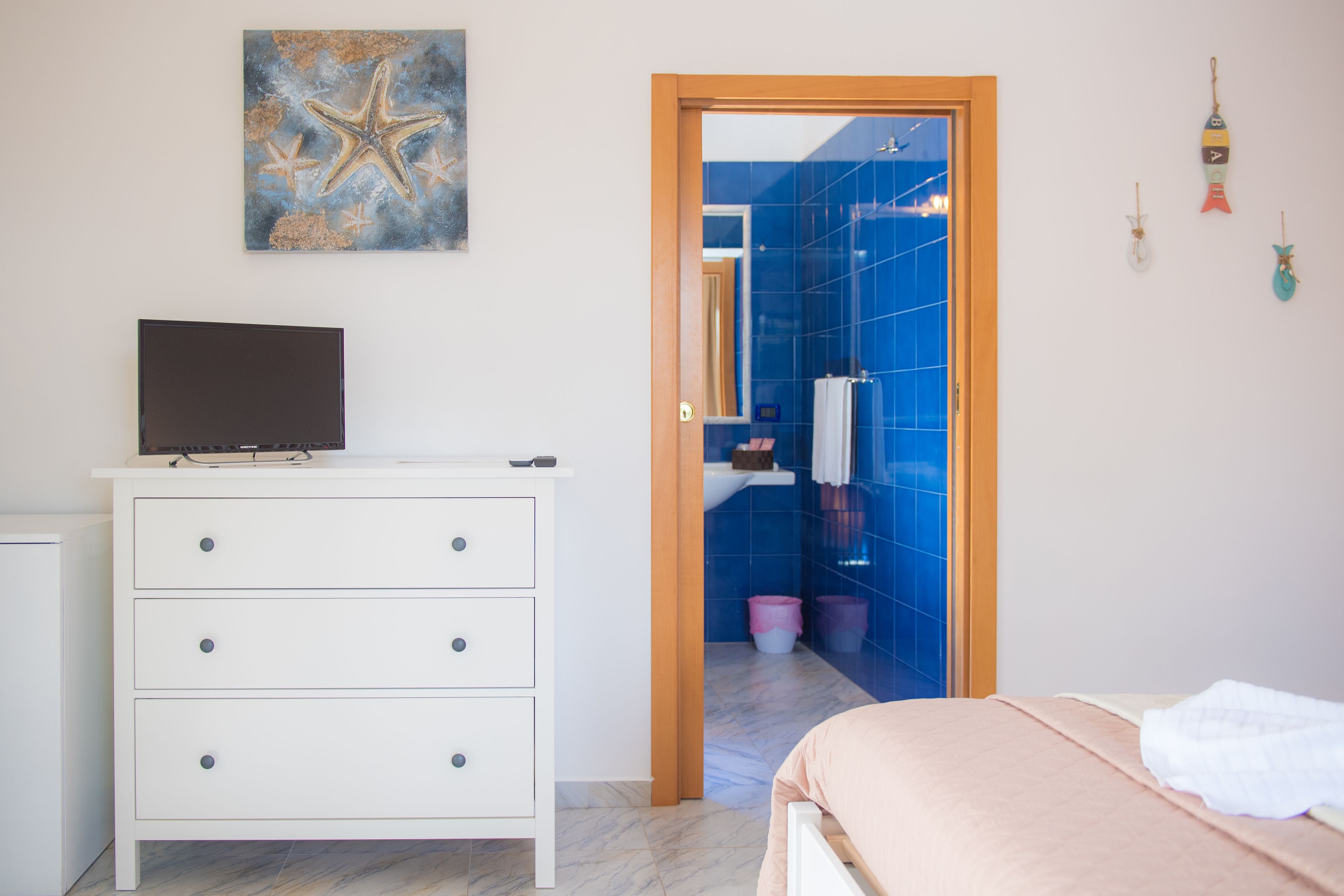 Un dormitorio con una cama, un aparador, un televisor sobre el aparador y un baño visible a través de una puerta abierta.