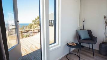 Ein Zimmer mit einem großen Fenster, einem Sessel mit Kissen, einem kleinen Tisch und einem Blumentopf.