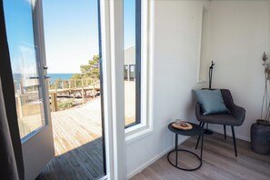 A room with a large window, a chair with a cushion, a small table, and a potted plant.