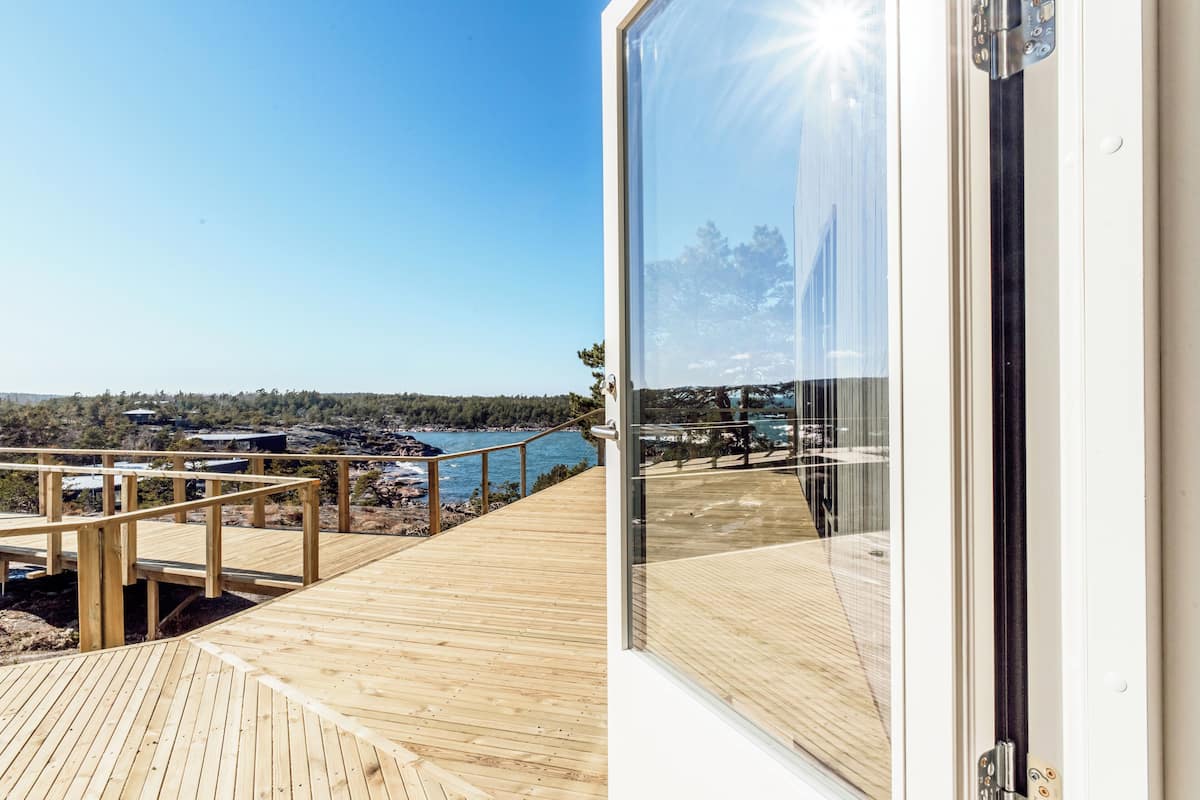 A wooden deck with a glass door leading to a view of a body of water and distant land.