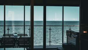 A room with large windows overlooking the sea, a table with chairs, and a bench.