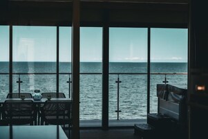 Una habitación con amplios ventanales con vistas al mar, una mesa con sillas y un banco.