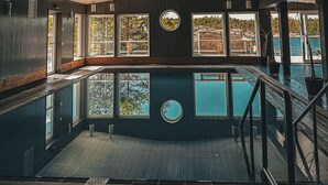 A pool area with a wooden deck, a pool, and large windows offering views of the outdoors.