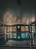 Un área de piscina con terraza de madera, piscina y ventanas amplias que ofrecen vistas al exterior.