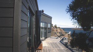 A modern building with a balcony overlooking the sea, featuring a wooden deck and a glass door.