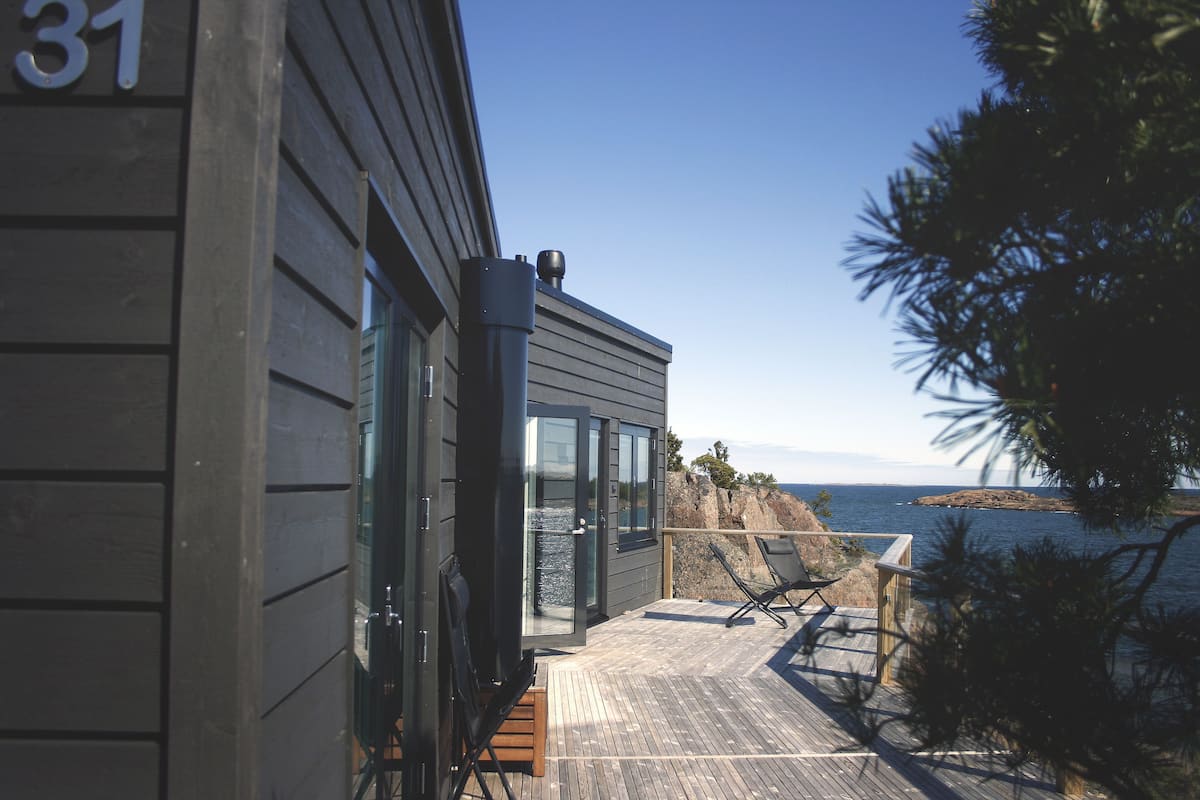 A modern building with a balcony overlooking the sea, featuring a wooden deck and a glass door.