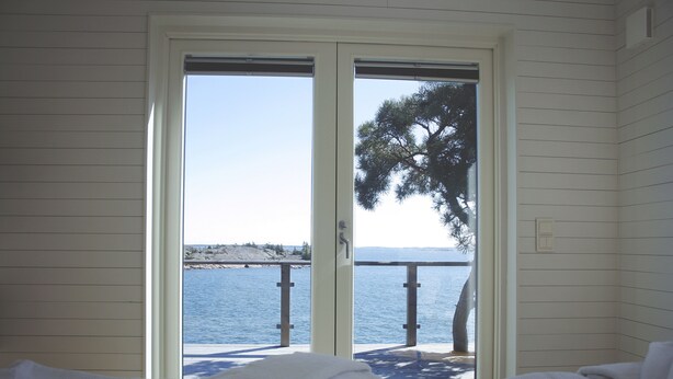 A room with a bed and a view of the sea through a sliding door.