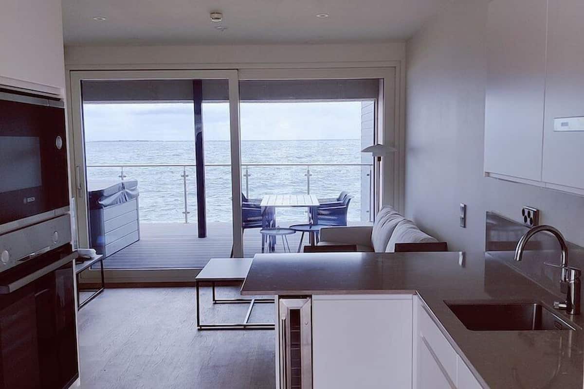 A modern kitchen with a view of the sea, a dining area with a table and chairs, and a large sliding glass door leading to an outdoor seating area.