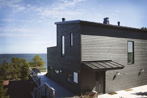 Un edificio moderno de dos pisos con una terraza con vistas al mar, que presenta un diseño minimalista y grandes ventanales.
