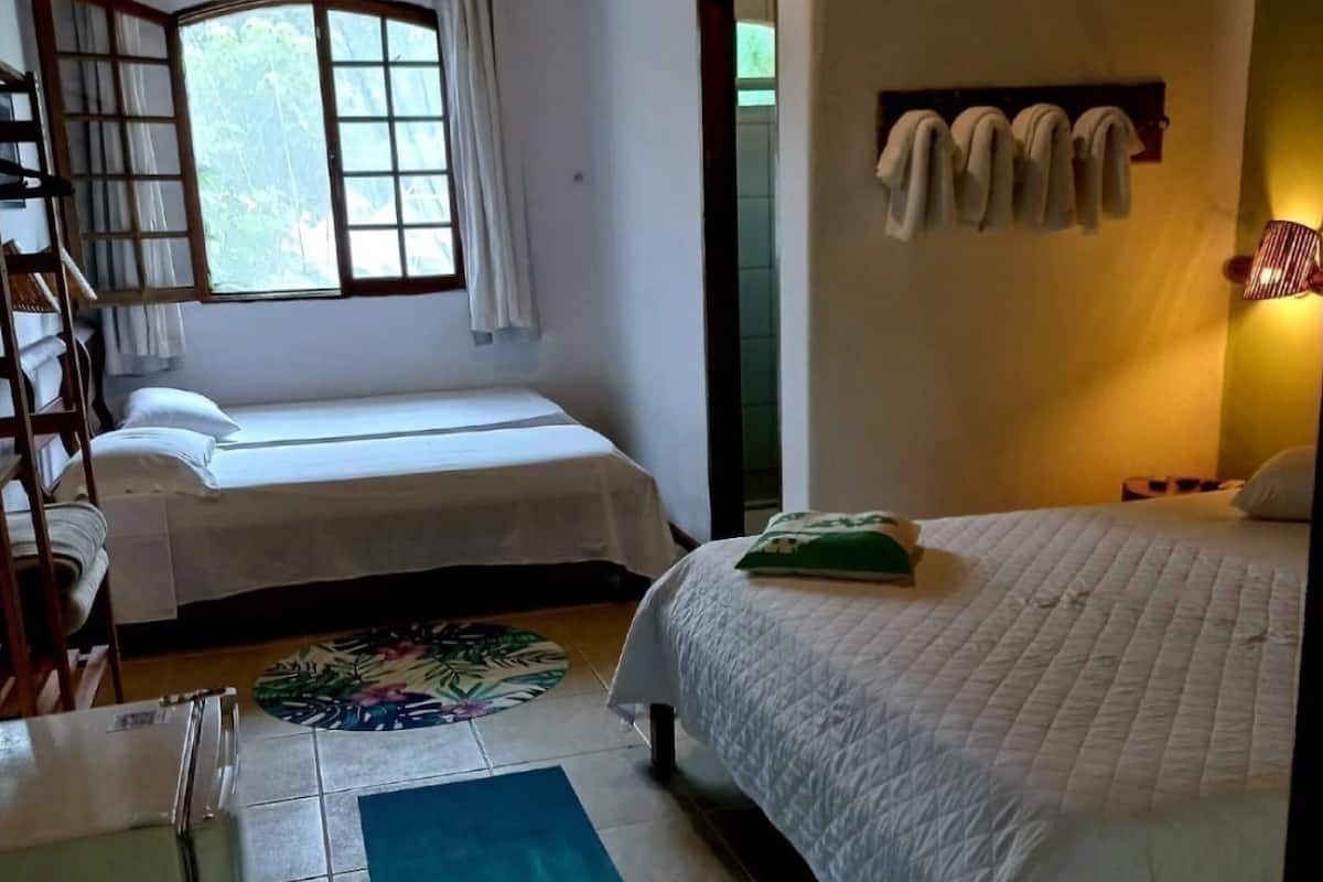 Una habitación con dos camas, una ventana con cortinas, techo de madera y suelo de baldosas.