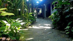 A narrow stone pathway flanked by lush green foliage, leading to a building with a thatched roof. - Pousada Magia Verde (Paraty)