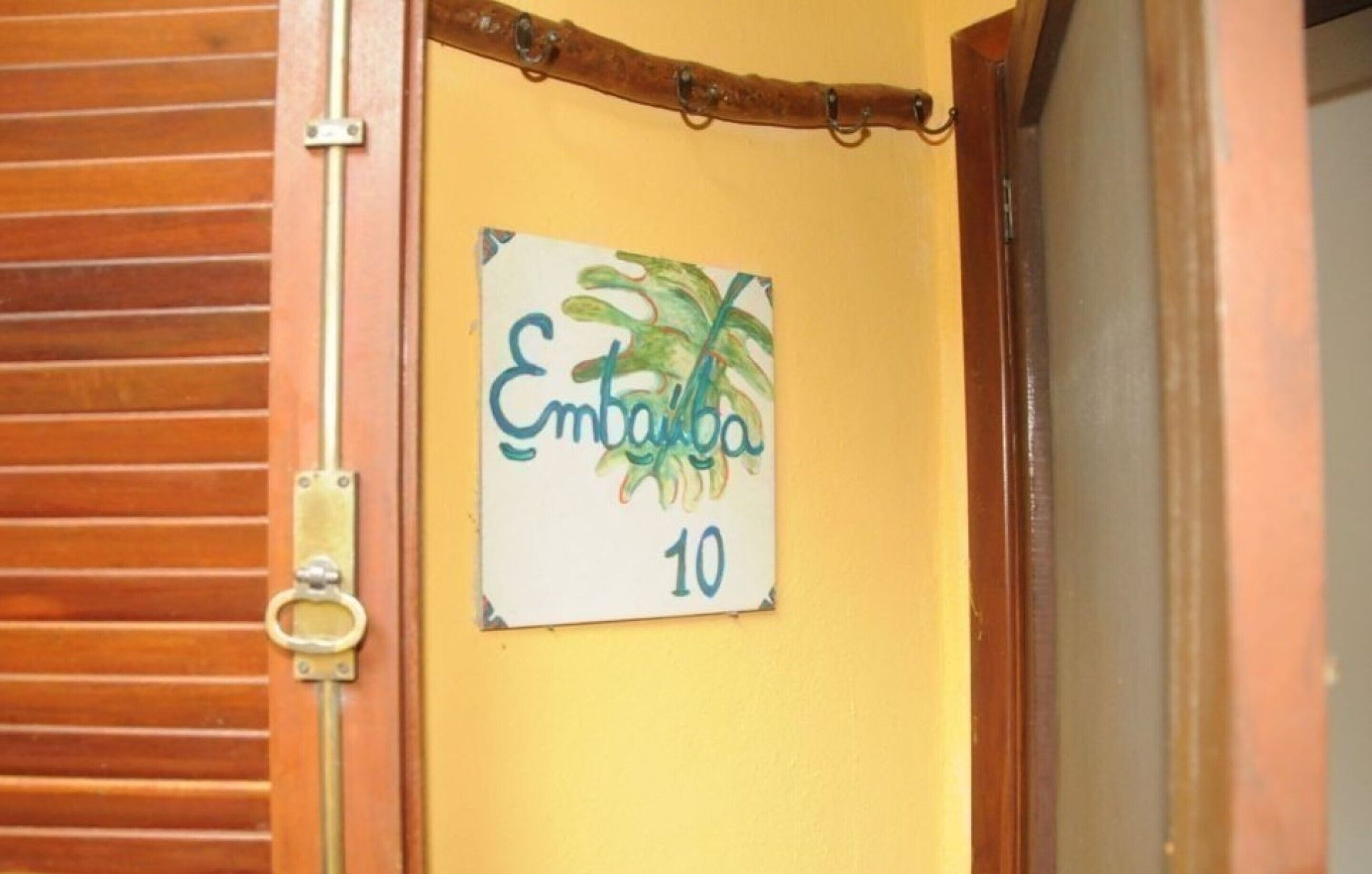Een deur met een bordje waarop 'Embaiba 10' staat, tegen een gele muur.