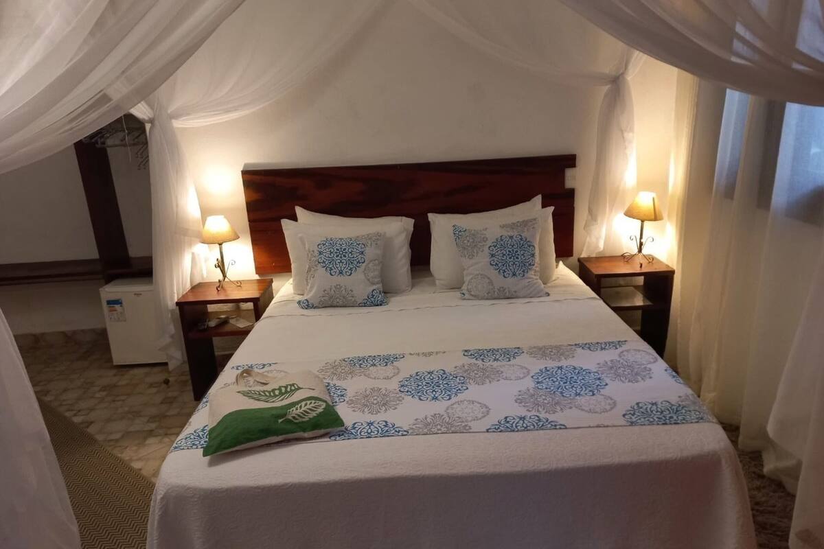 Una cama con dosel, dos lámparas de noche y una colcha estampada.