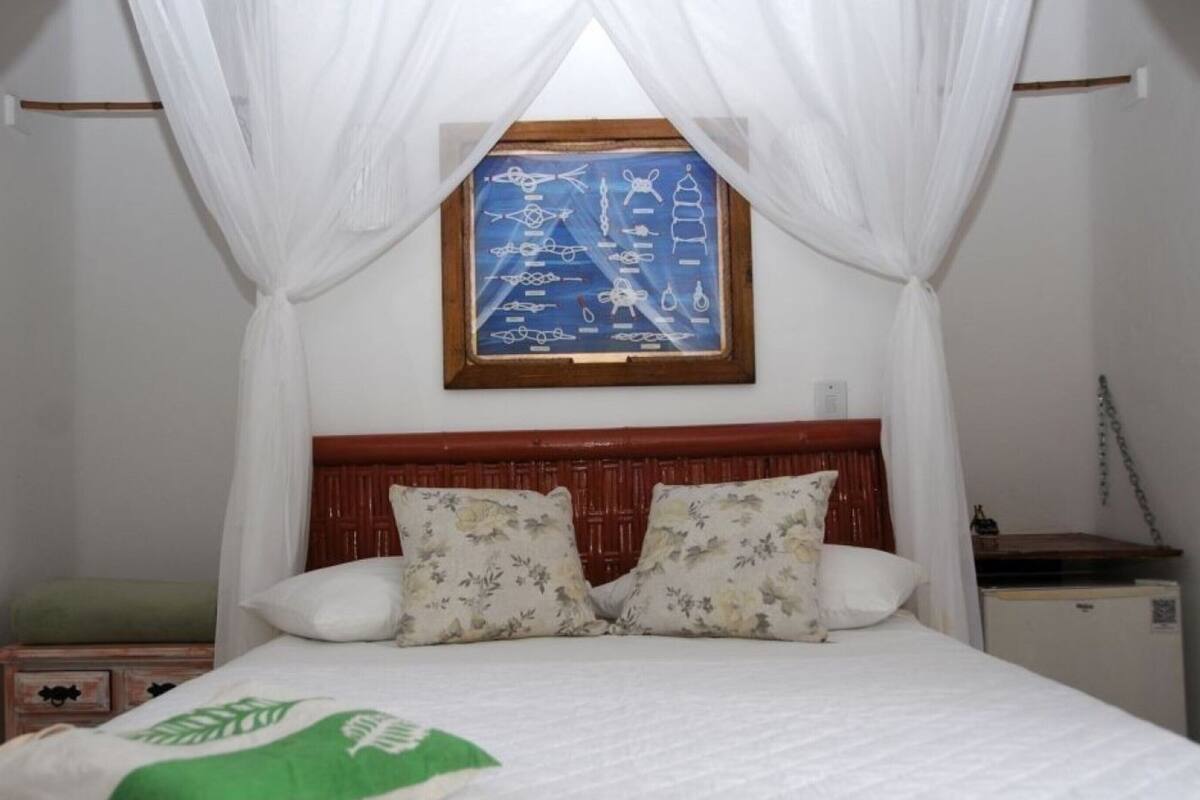 Una cama con ropa de cama blanca, cabecera de madera y una ventana con marco azul.