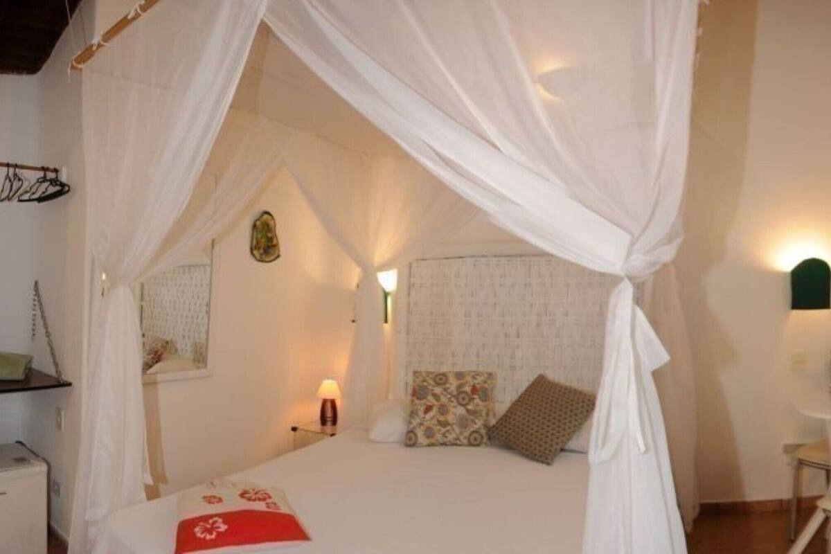 Un dormitorio con cama con dosel, una mesita de noche con lámpara, una silla y una pequeña mesa con lámpara.