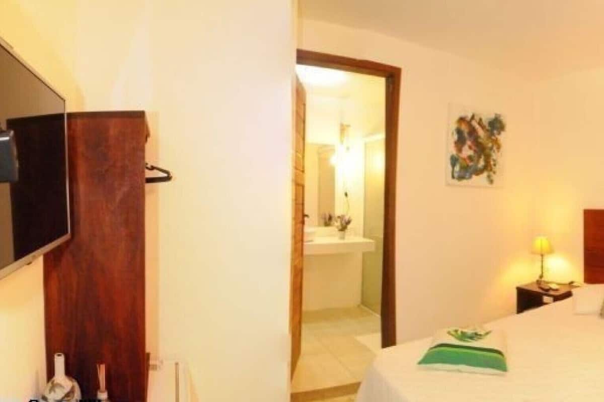 Habitación de hotel con cabecera de madera, dos mesitas de noche con lámparas, una cama con almohadas, una pequeña mesa con una silla y un espejo en la pared.