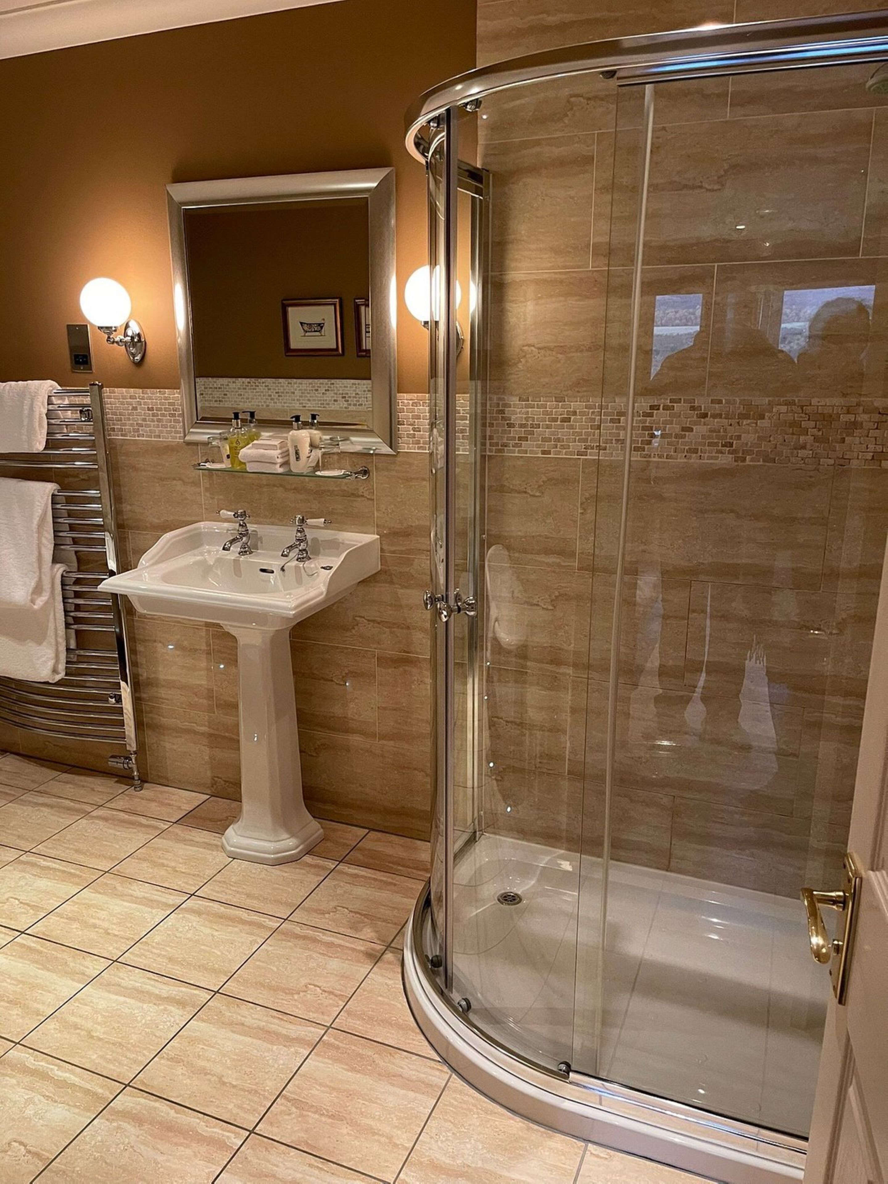 A bathroom with a glass-enclosed shower, a pedestal sink, and a towel rack.