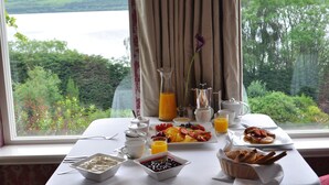 Een ontbijttafel met uitzicht op een schilderachtig meer, inclusief een fruitschaal, koffie en sap.