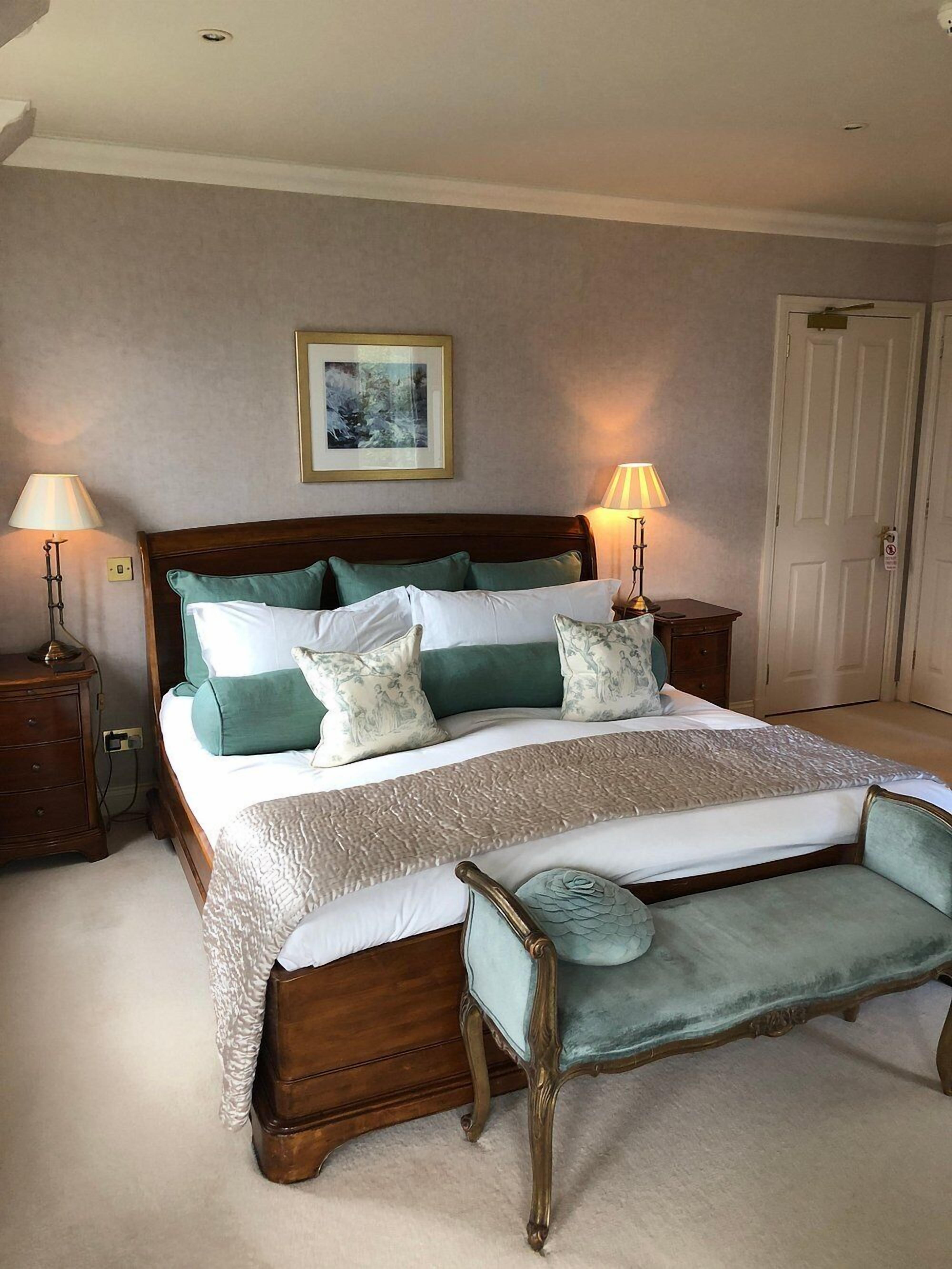 A bedroom with a large bed, two bedside tables, a bench, a framed picture on the wall, and a door.