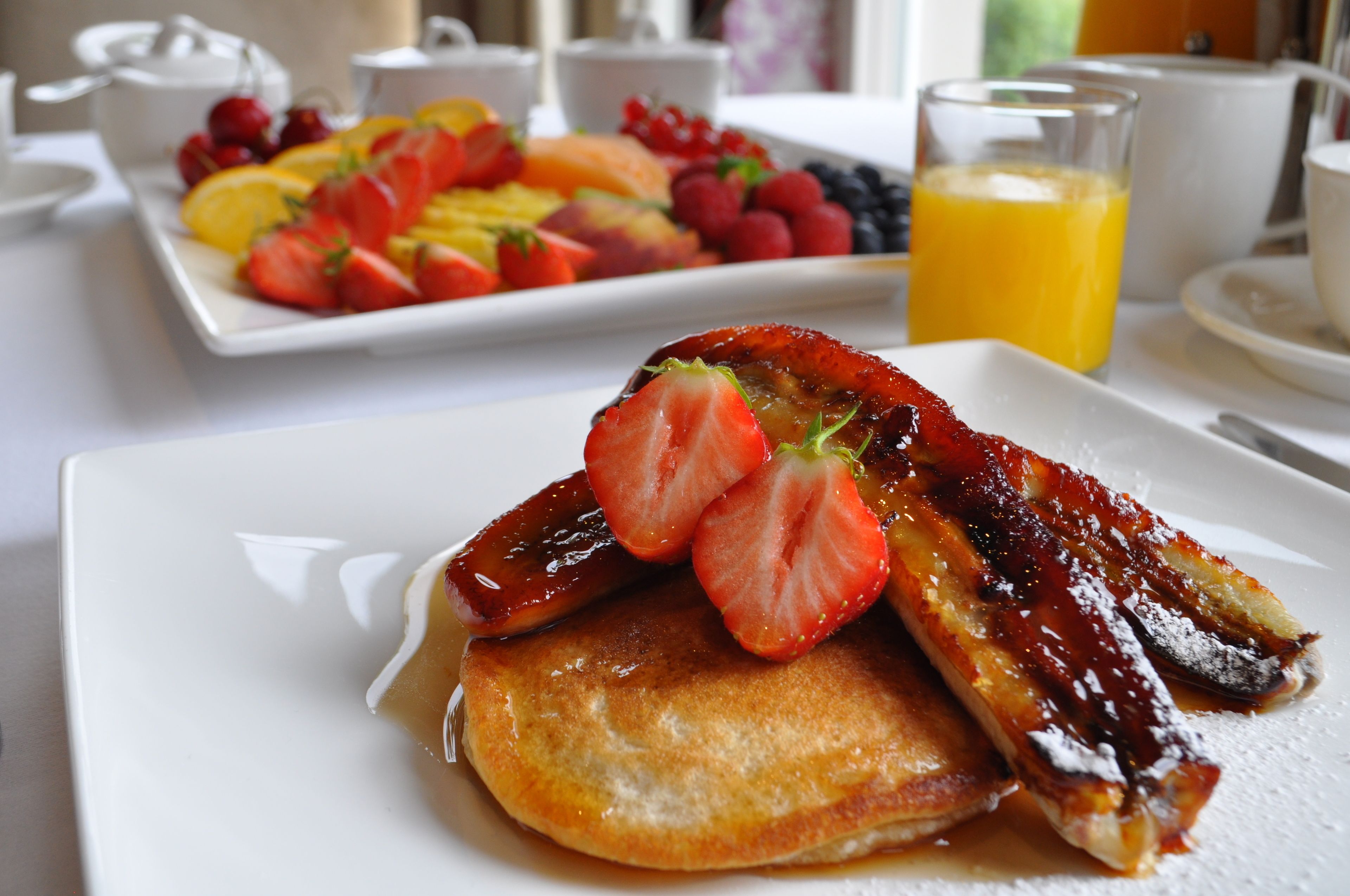 A breakfast plate with pancakes, strawberries, and a glass of orange juice.