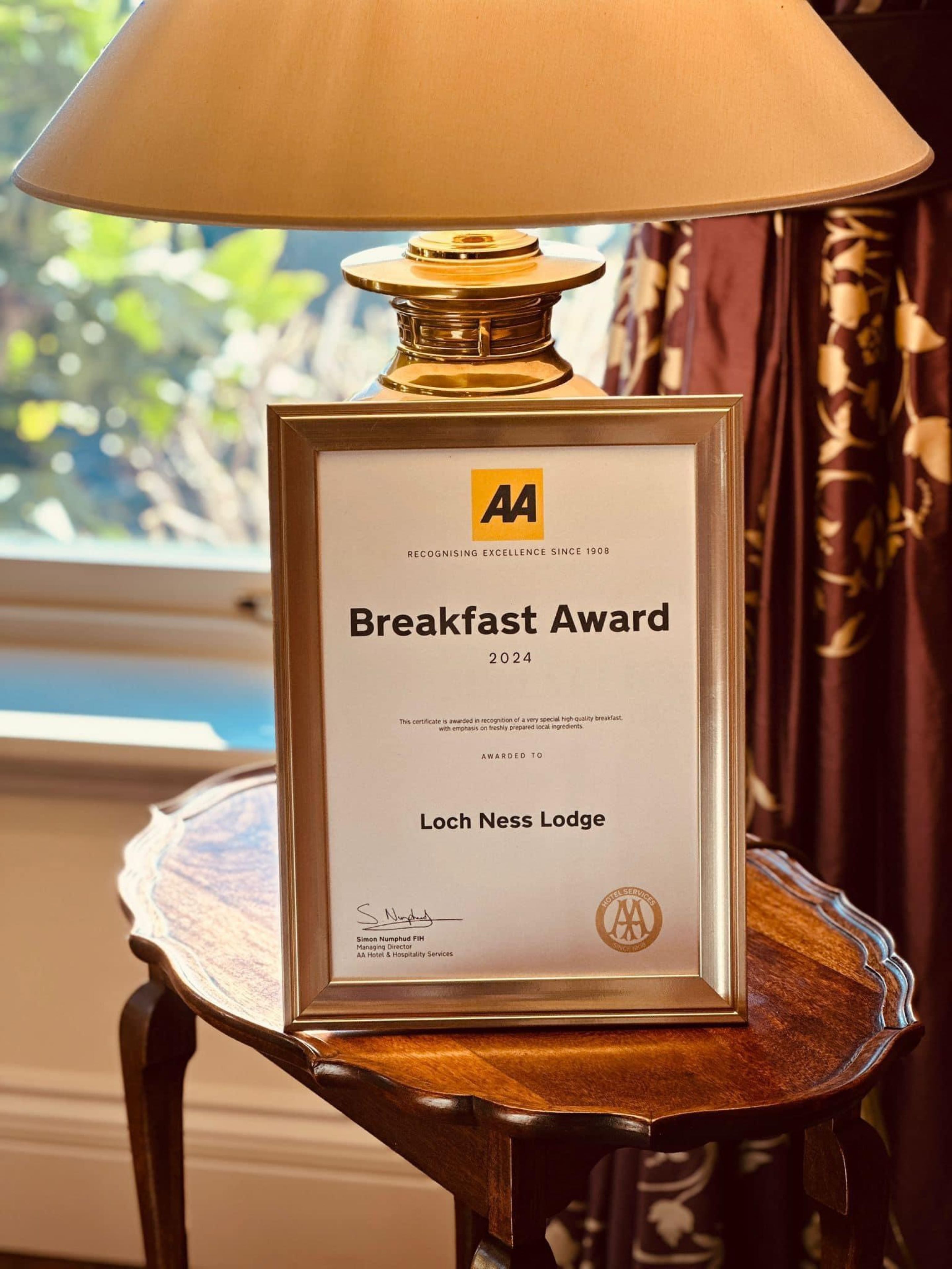 A framed certificate on a table with a lamp, indicating a Breakfast Award for 2024 awarded to Loch Ness Lodge.