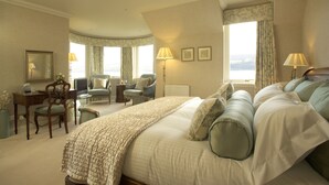 Een hotelkamer met een groot bed, twee fauteuils, een bureau en uitzicht op zee.