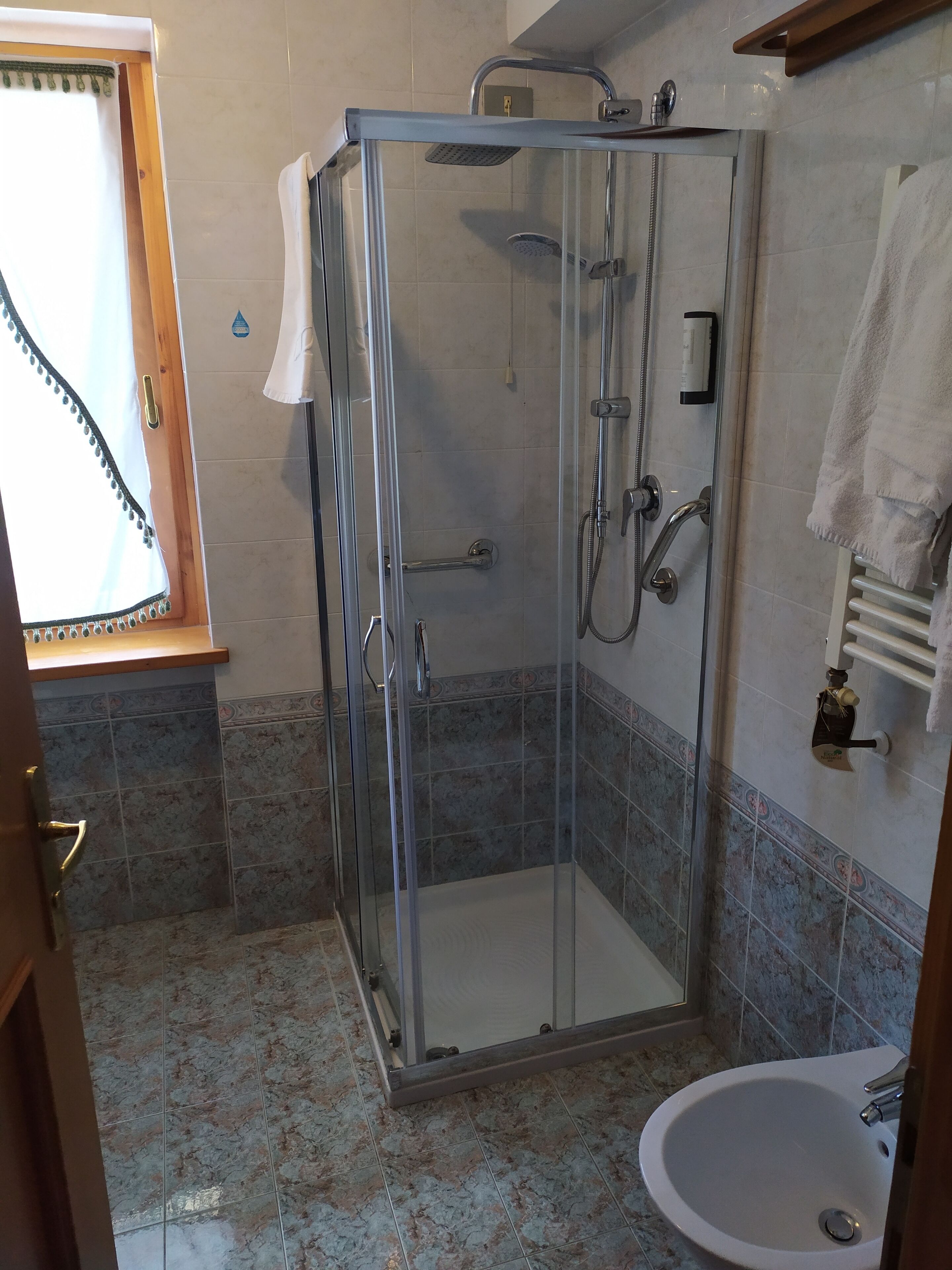 Ducha envuelta en vidrio con cabezal de ducha de mano y grifo empotrado.