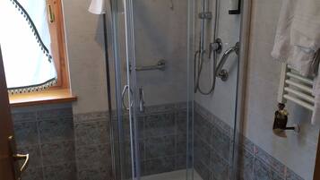 Ducha envuelta en vidrio con cabezal de ducha de mano y grifo empotrado.