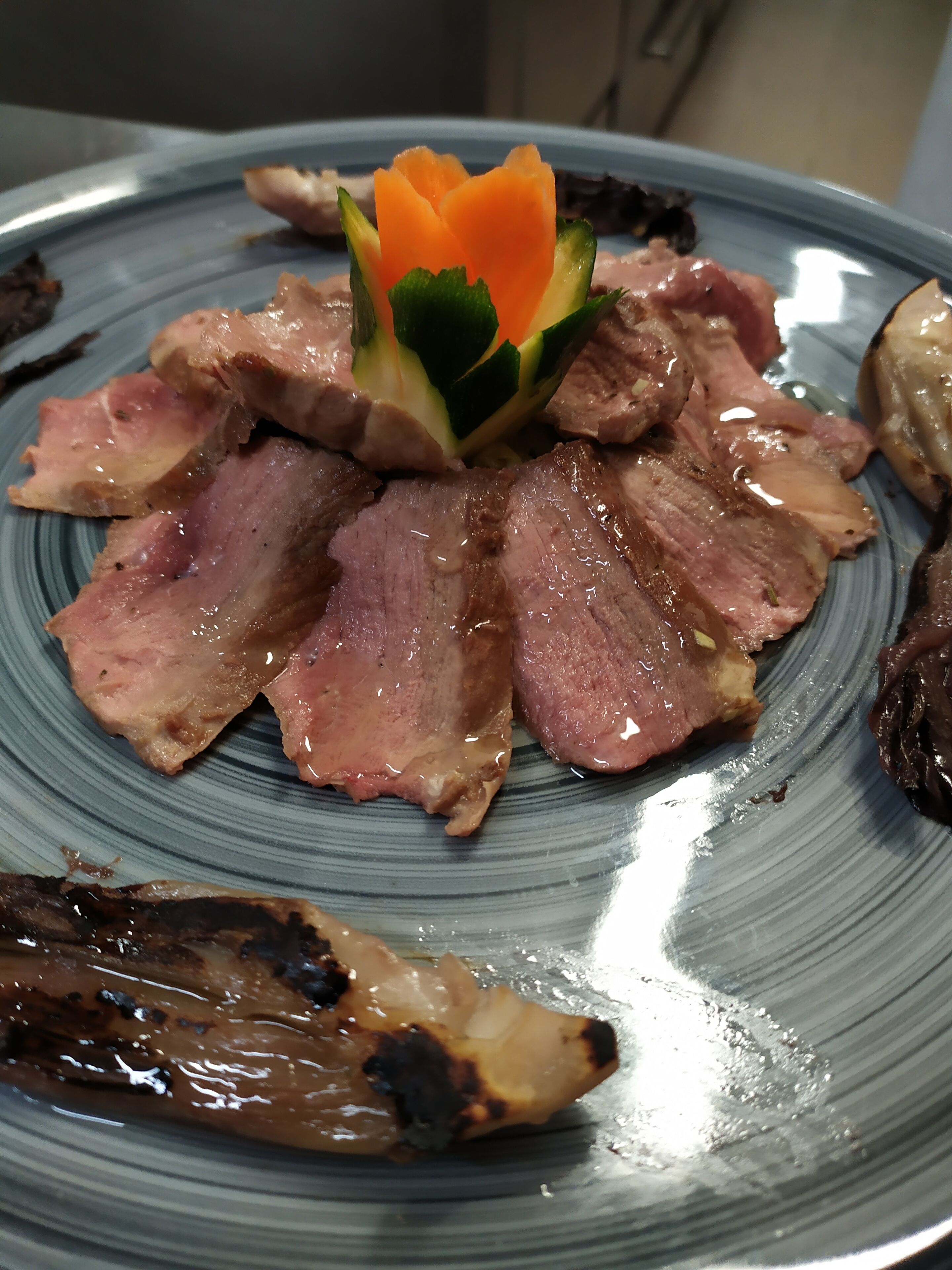 A plate with sliced meat and a decorative vegetable arrangement.