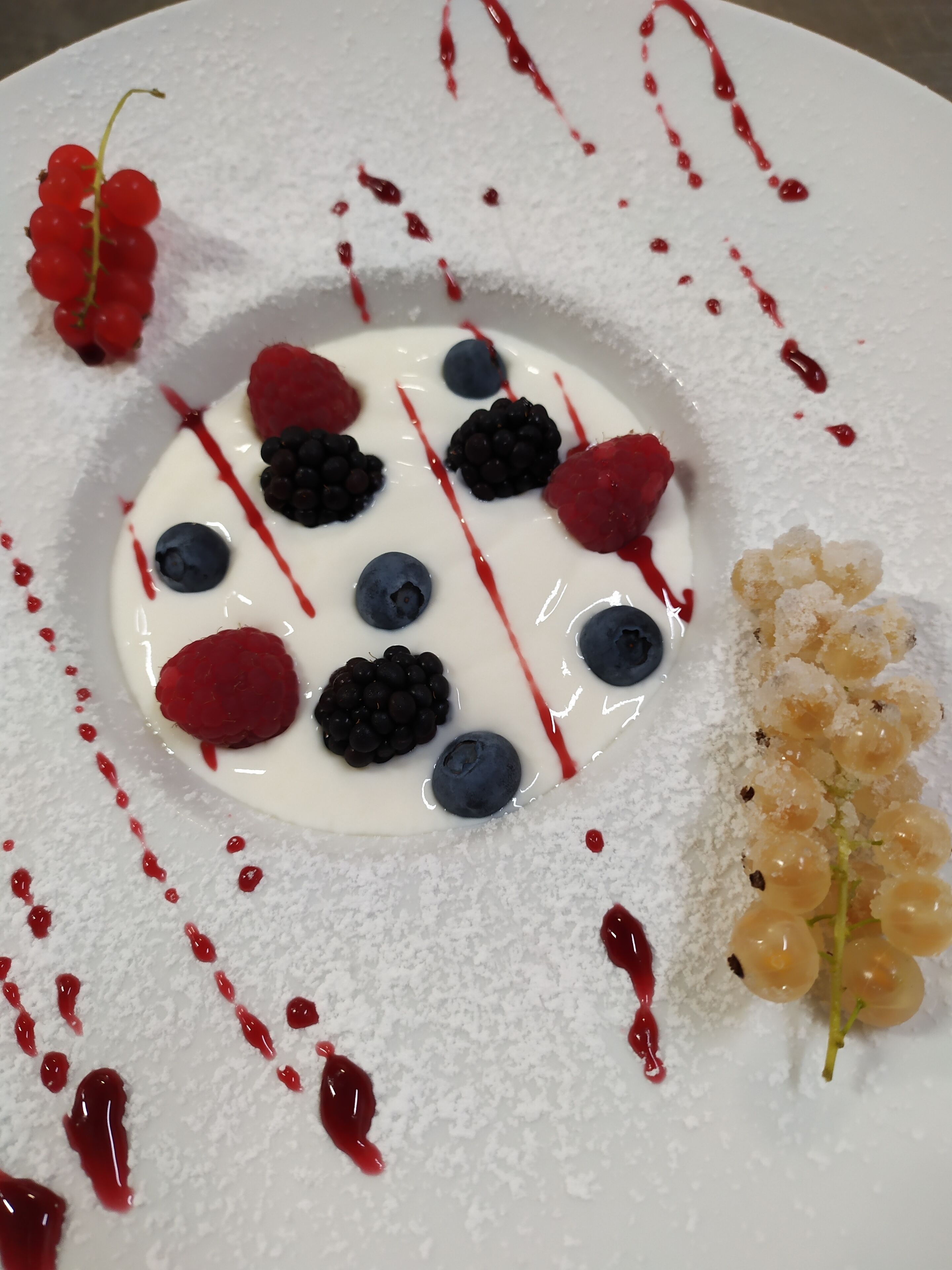 Un postre con bayas y uvas sobre un plato blanco.