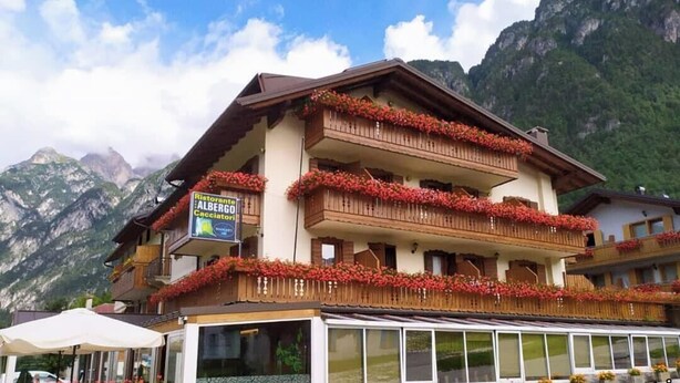 A multi-story building with balconies adorned with red flowers, a sign for 'Ristorante Albergo Cacciatori', and a mountain backdrop. - Albergo Ristorante Cacciatori  (Auronzo di Cadore)