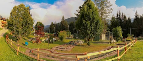 A miniature golf course with a wooden fence, green grass, and trees in the background.