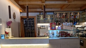 A bar area with a wooden counter, shelves with bottles, and a coffee machine. - Albergo Ristorante Cacciatori  (Auronzo di Cadore)