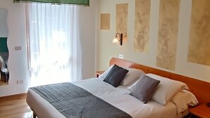 A bedroom with a large bed, a wooden floor, a green throw blanket, and a nightstand with a lamp. - Albergo Ristorante Cacciatori  (Auronzo di Cadore)