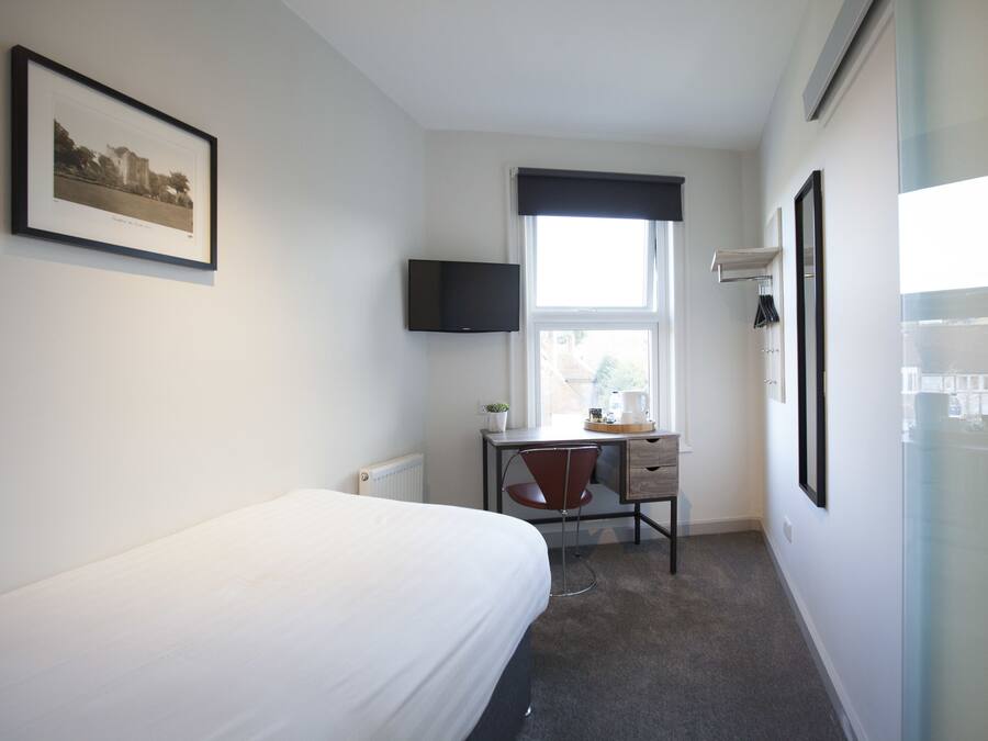 A hotel room with a bed, a desk with a chair, a television, and a window with a view of buildings.
