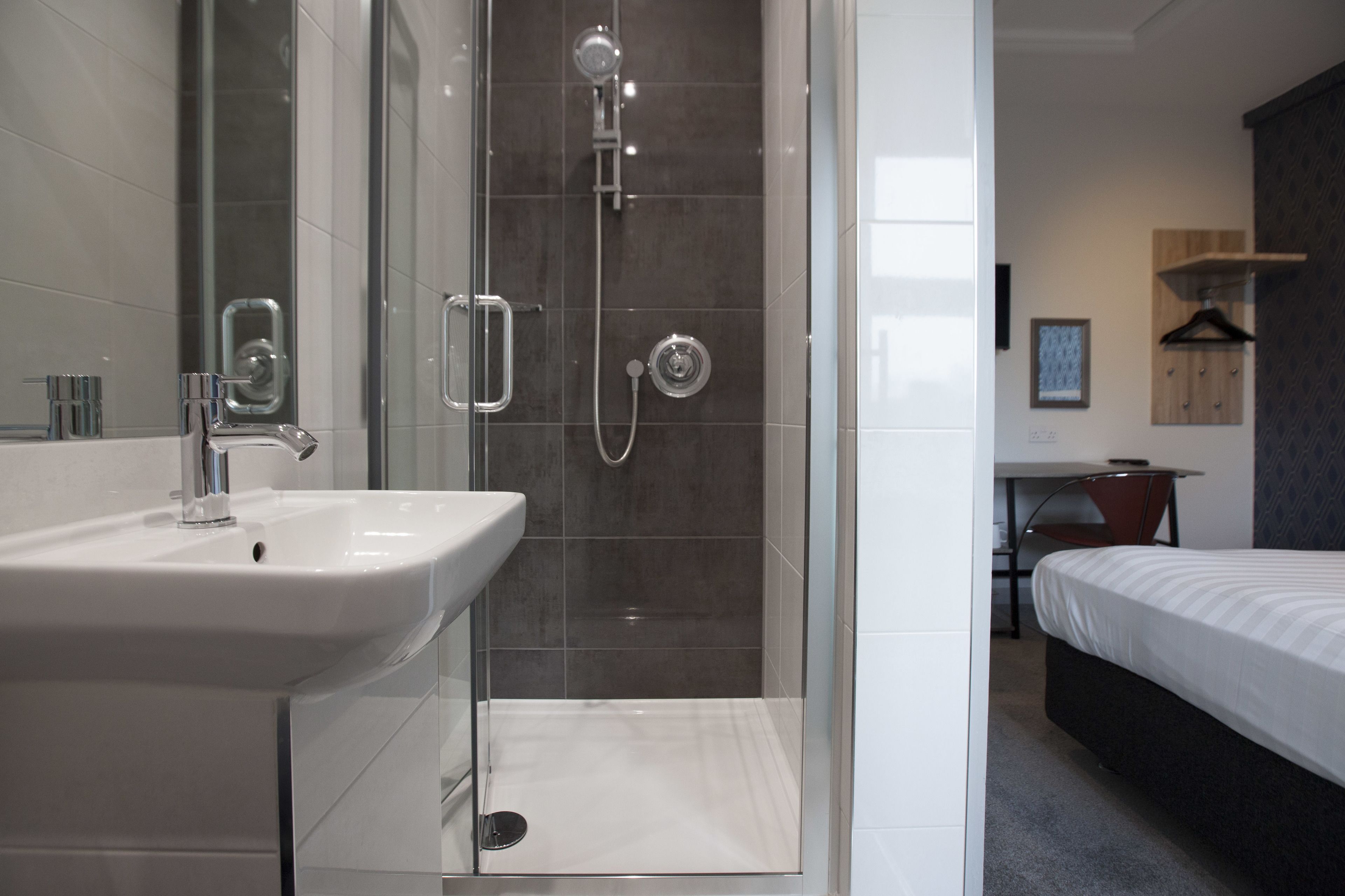 A modern bathroom with a glass-enclosed shower, a white sink, and a small table with a chair.