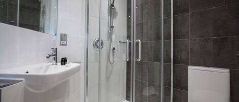 A modern bathroom with a glass-enclosed shower, a white sink, and a toilet.