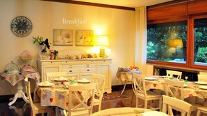 A breakfast setting with multiple tables and chairs, a clock on the wall, and a window with a view of greenery. - Villa Bianca (Sona)