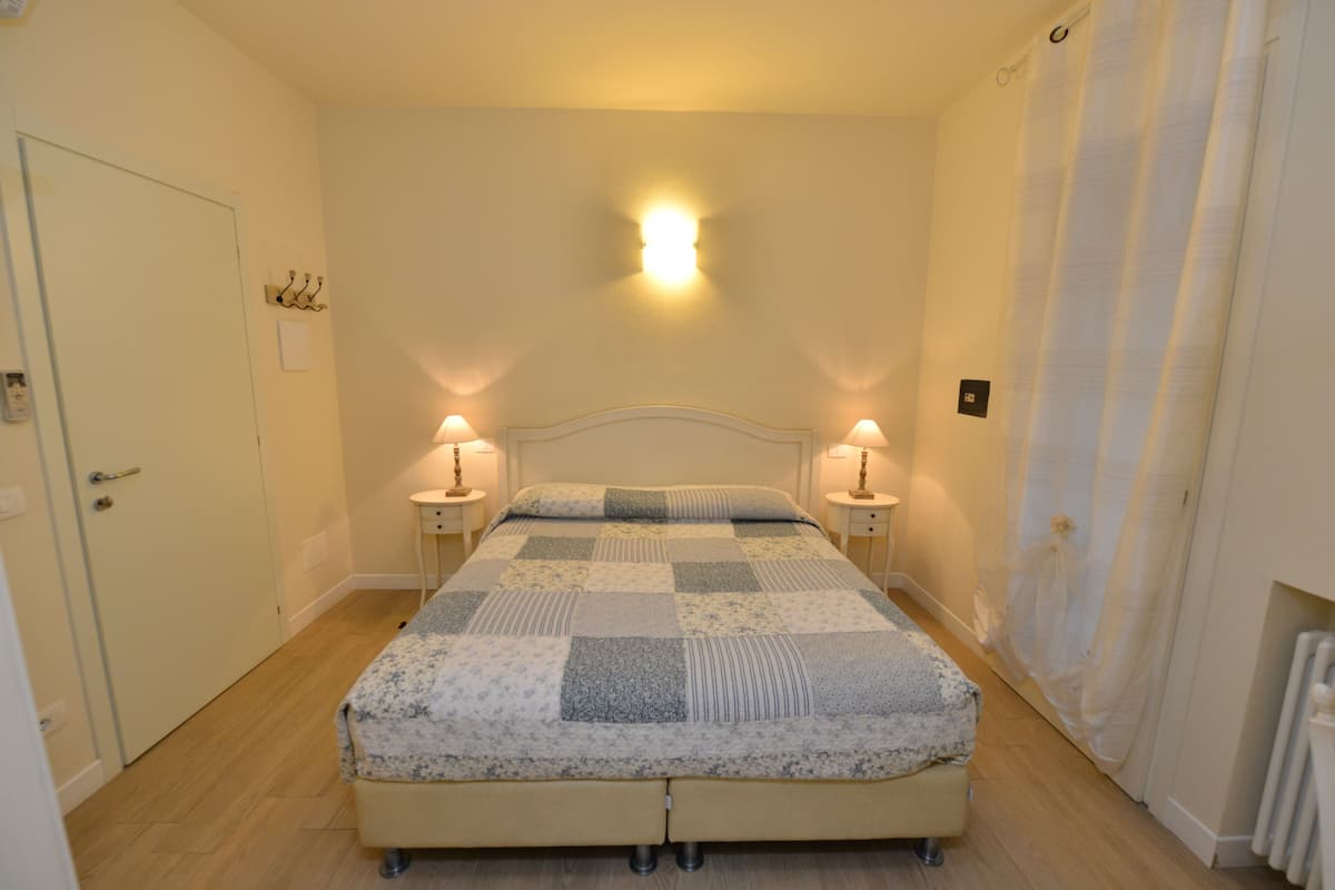 Ein Schlafzimmer mit einem Bett, zwei Nachttischlampen, einem Nachttisch, einer Tür und einer Wandleuchte.