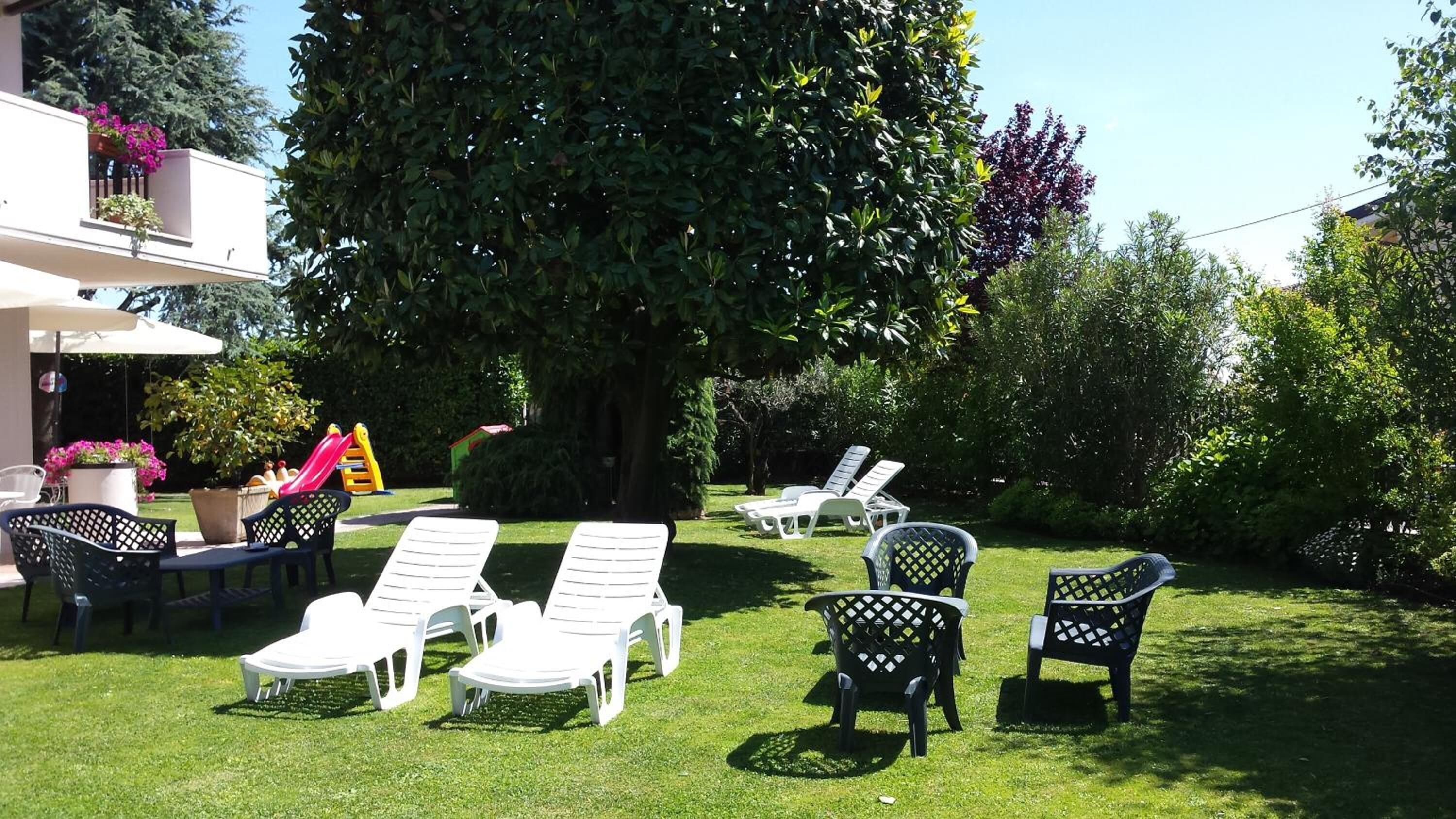 Un jardin avec des chaises longues blanches et un grand arbre.