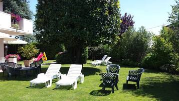Un jardin avec des chaises longues blanches et un grand arbre.