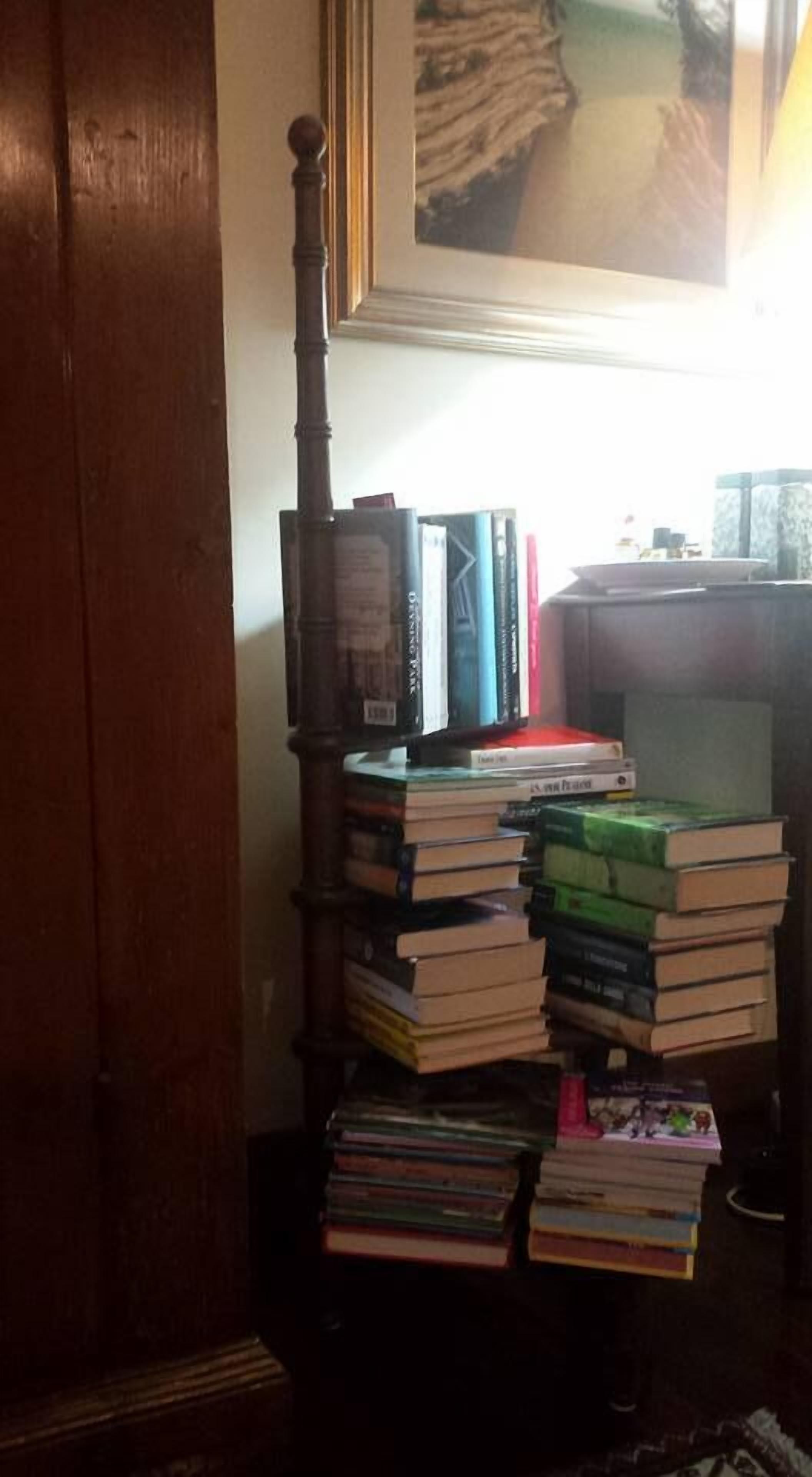 Een houten boekenplank vol boeken, geplaatst tegen een muur met daarboven een lijst met een foto.