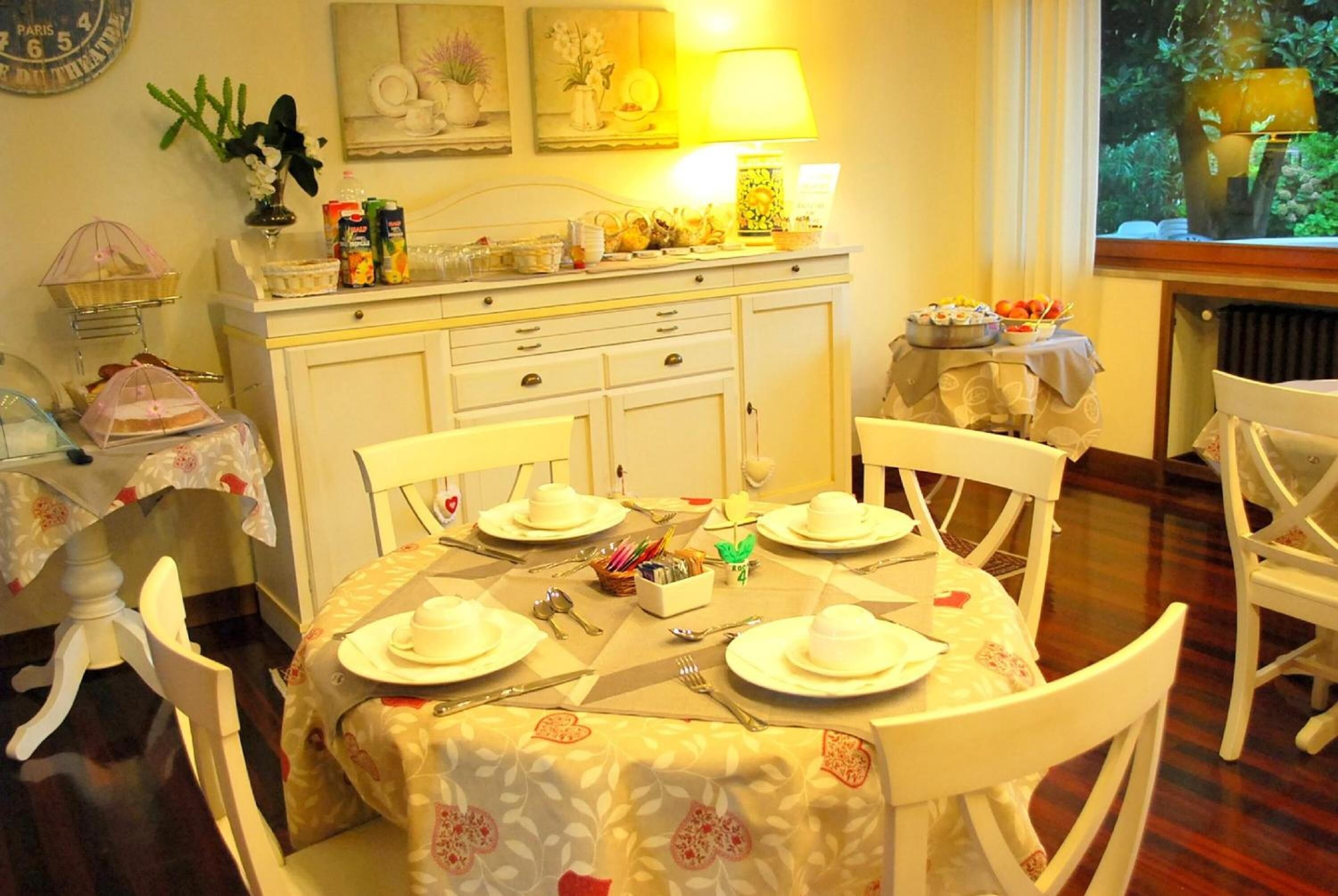 Une salle à manger avec une table ronde dressée pour quatre personnes, des chaises blanches et un buffet blanc sur lequel sont disposés divers objets.