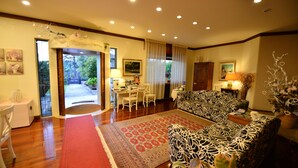 A spacious living room with a patterned sofa, a dining area with a table and chairs, and a red carpet leading to an open doorway. - Villa Bianca (Sona)