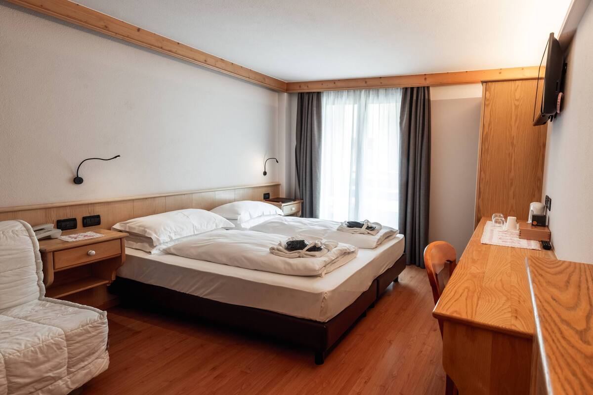 A hotel room with two beds, a wooden desk, a chair, a nightstand, and a TV mounted on the wall.
