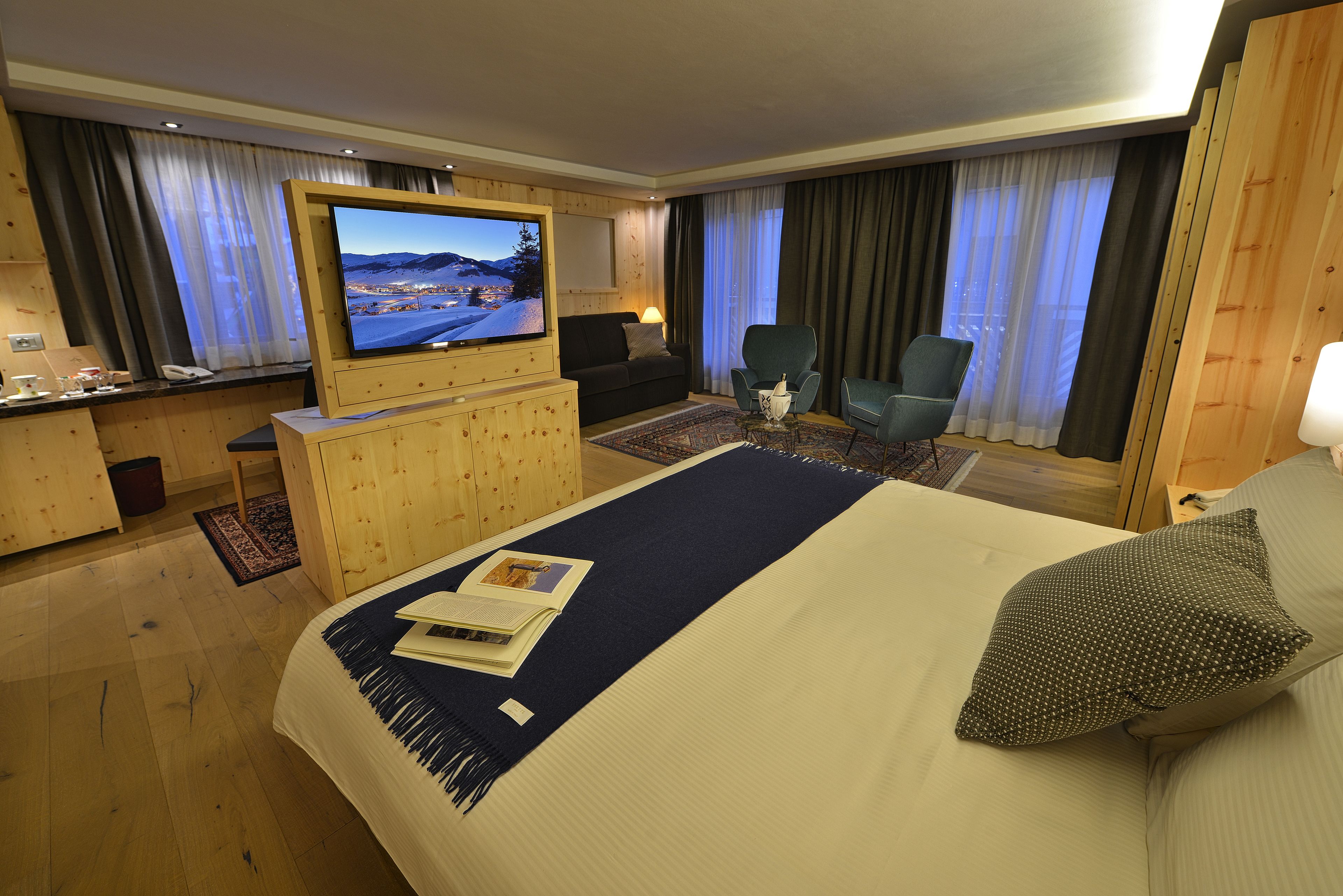 A hotel room with a large bed, a TV, a desk with a computer, and a view of the mountains.