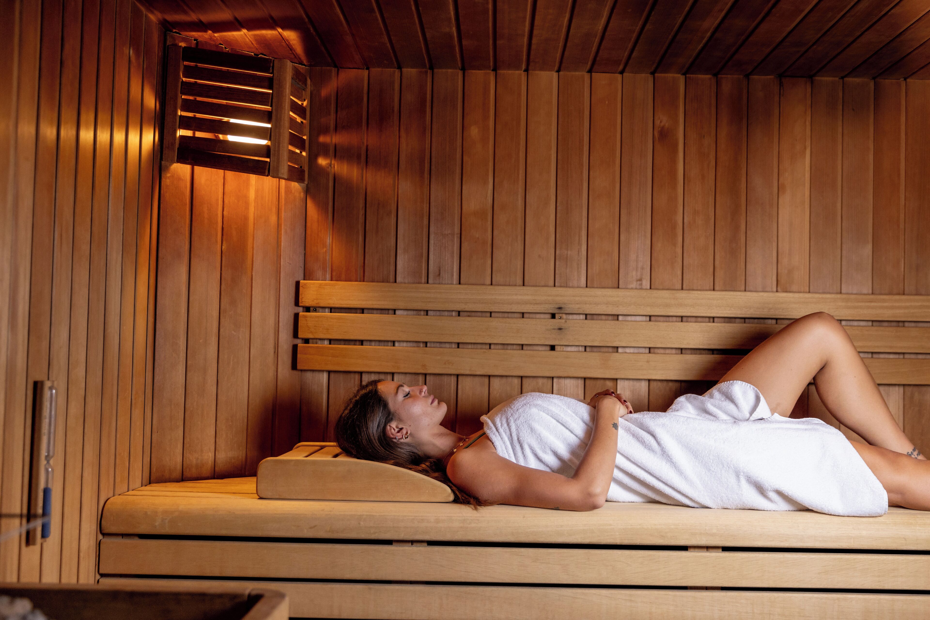 A wooden sauna with a bench and a person lying on it.