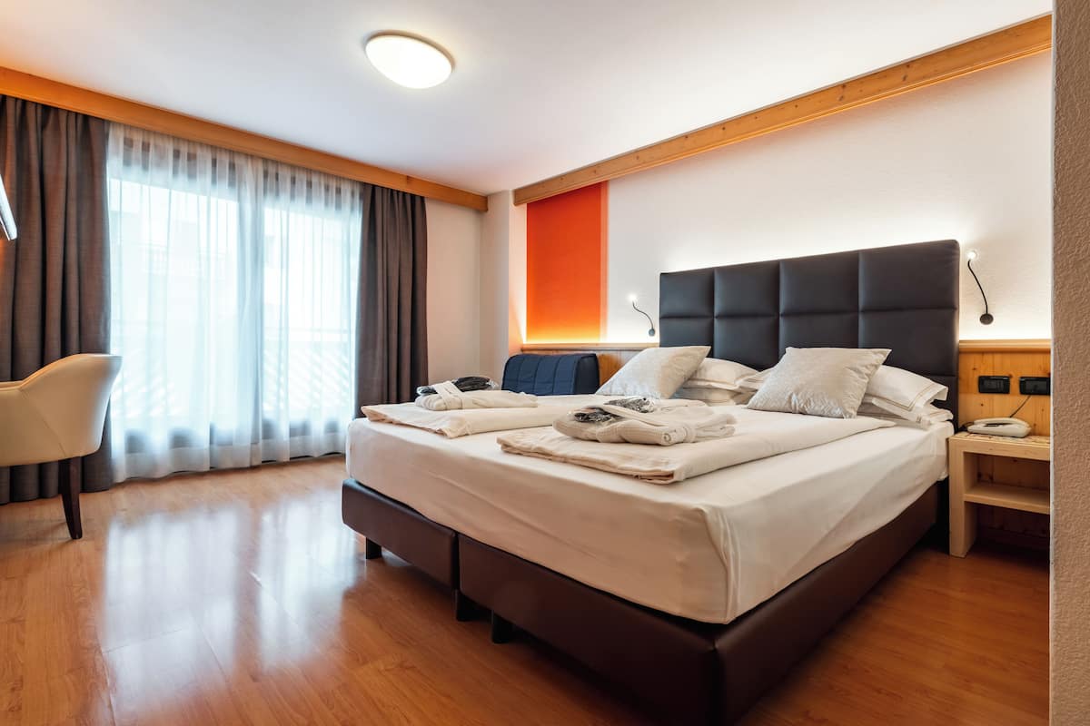 A modern hotel room with a large bed, a bedside table, a chair, and a large window with curtains.
