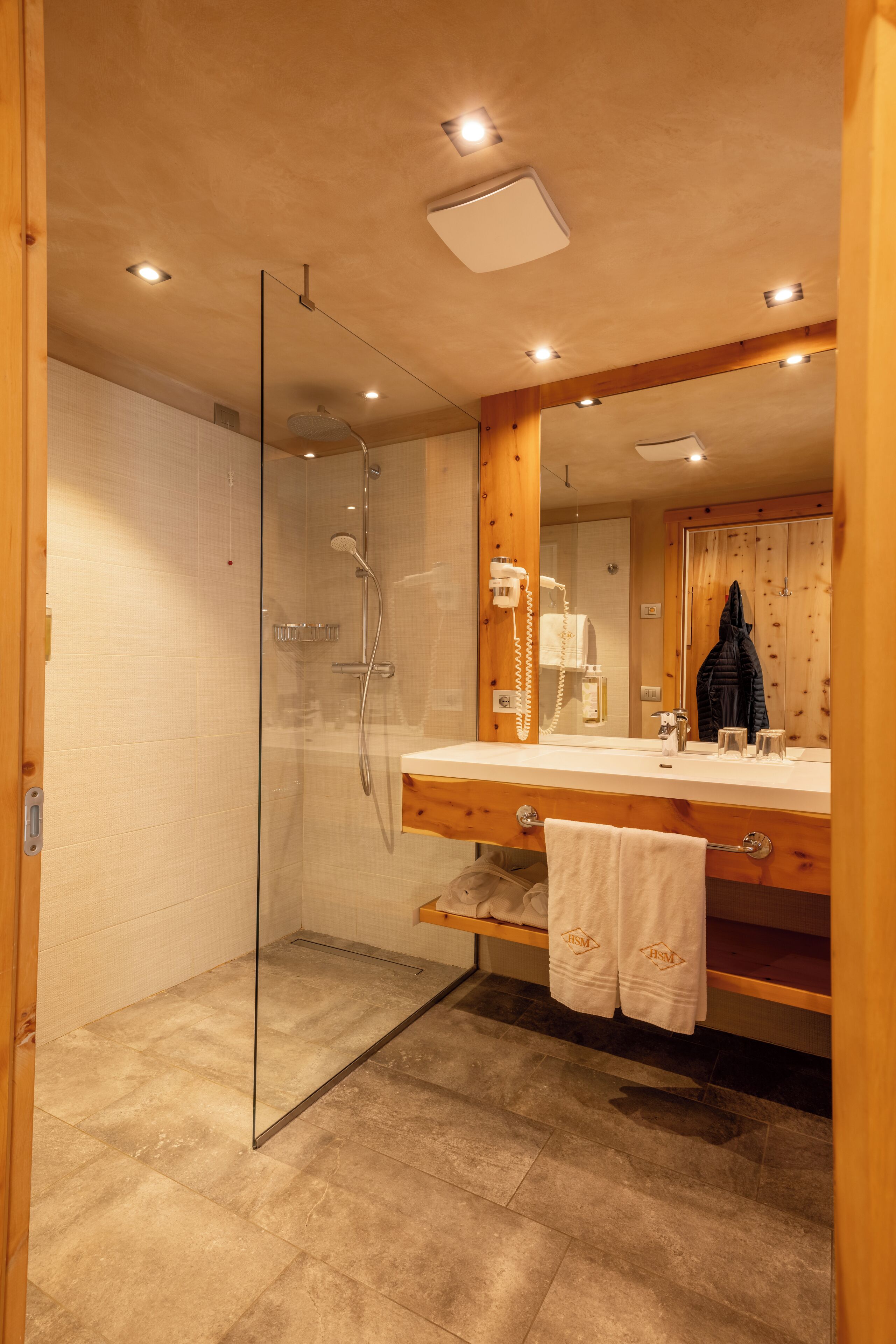 A modern bathroom with a glass-enclosed shower, a wooden vanity with a mirror, and a towel rack.
